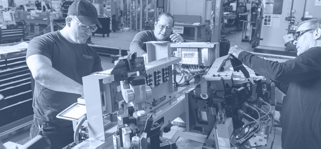 Three workers over viewing machine mechanisms